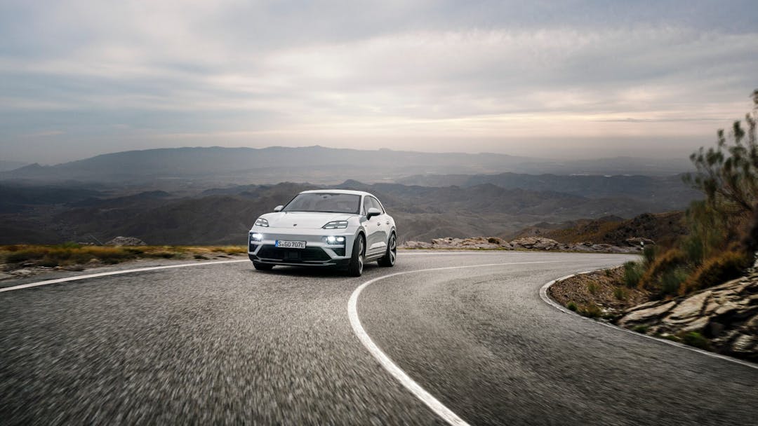 Porsche Macan in white front view driving with mountain range background