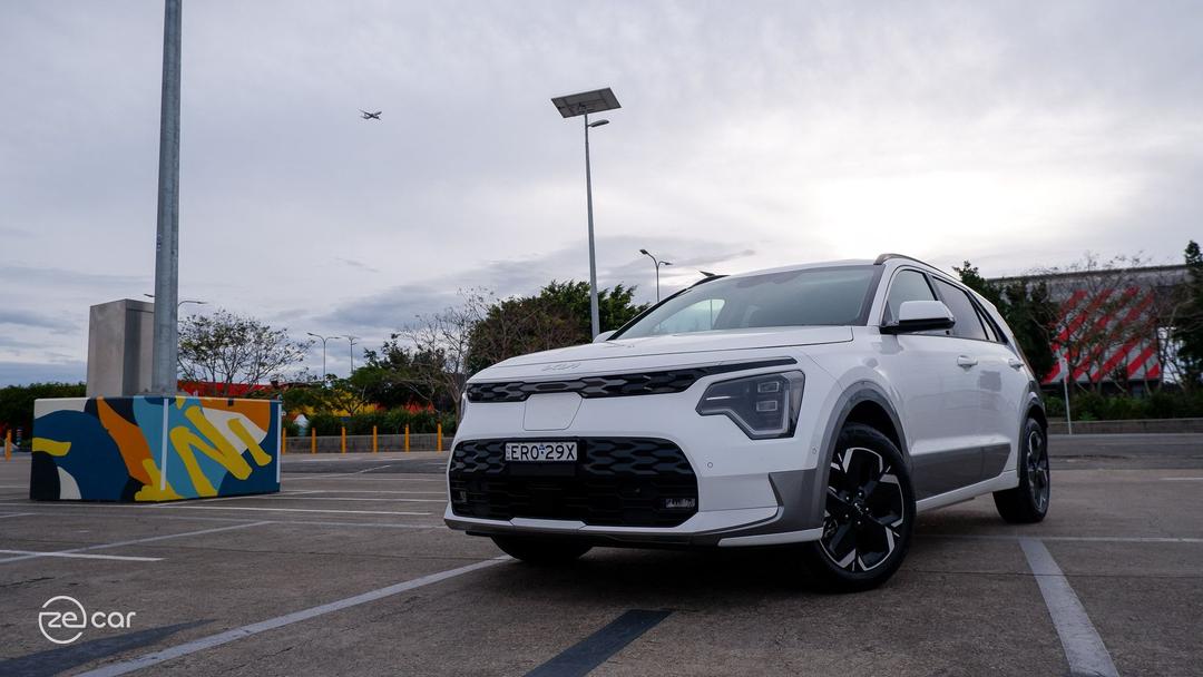 White Kia Niro EV in car park with aeroplane flying in sky