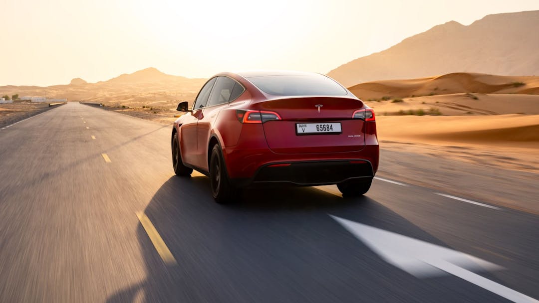 2024 Tesla Model Y in red rear view driving on highway with desert background 
