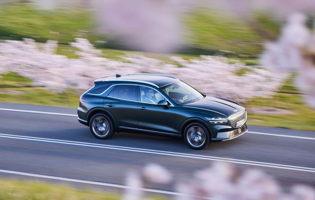 Green Genesis Electrified GV70 driving in front of flowers