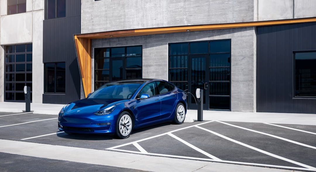 Blue Tesla Model Y charging from Destination Charger AC wall box in front of office building