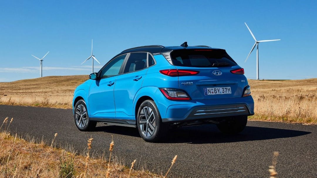 Blue and black roof Hyundai Kona Electric in front of wind turbines rear view