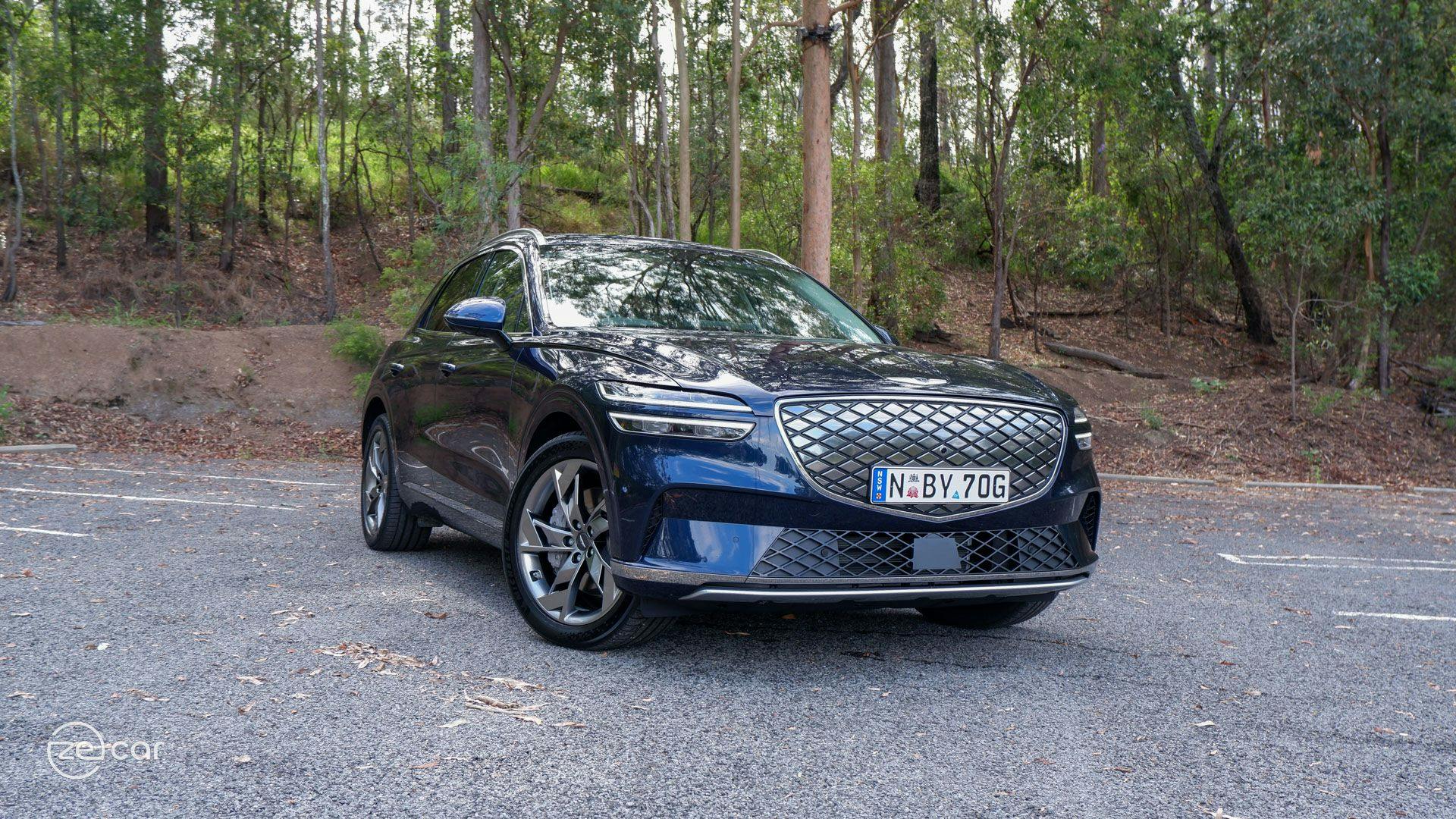 Dark blue Genesis Electrified GV70 in front of hiking forest