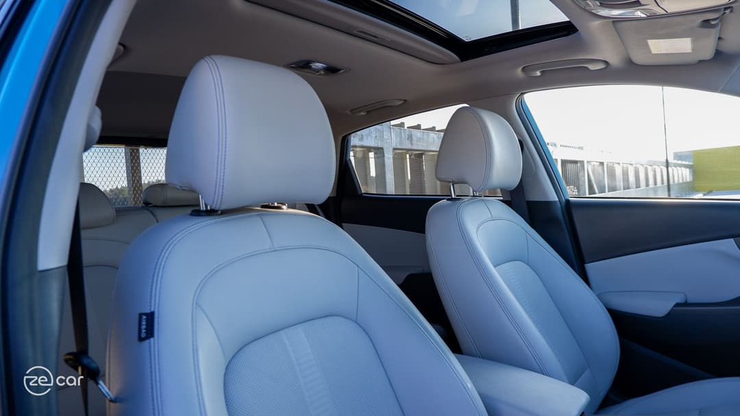 Hyundai Kona Electric driving in residential street and front white seats