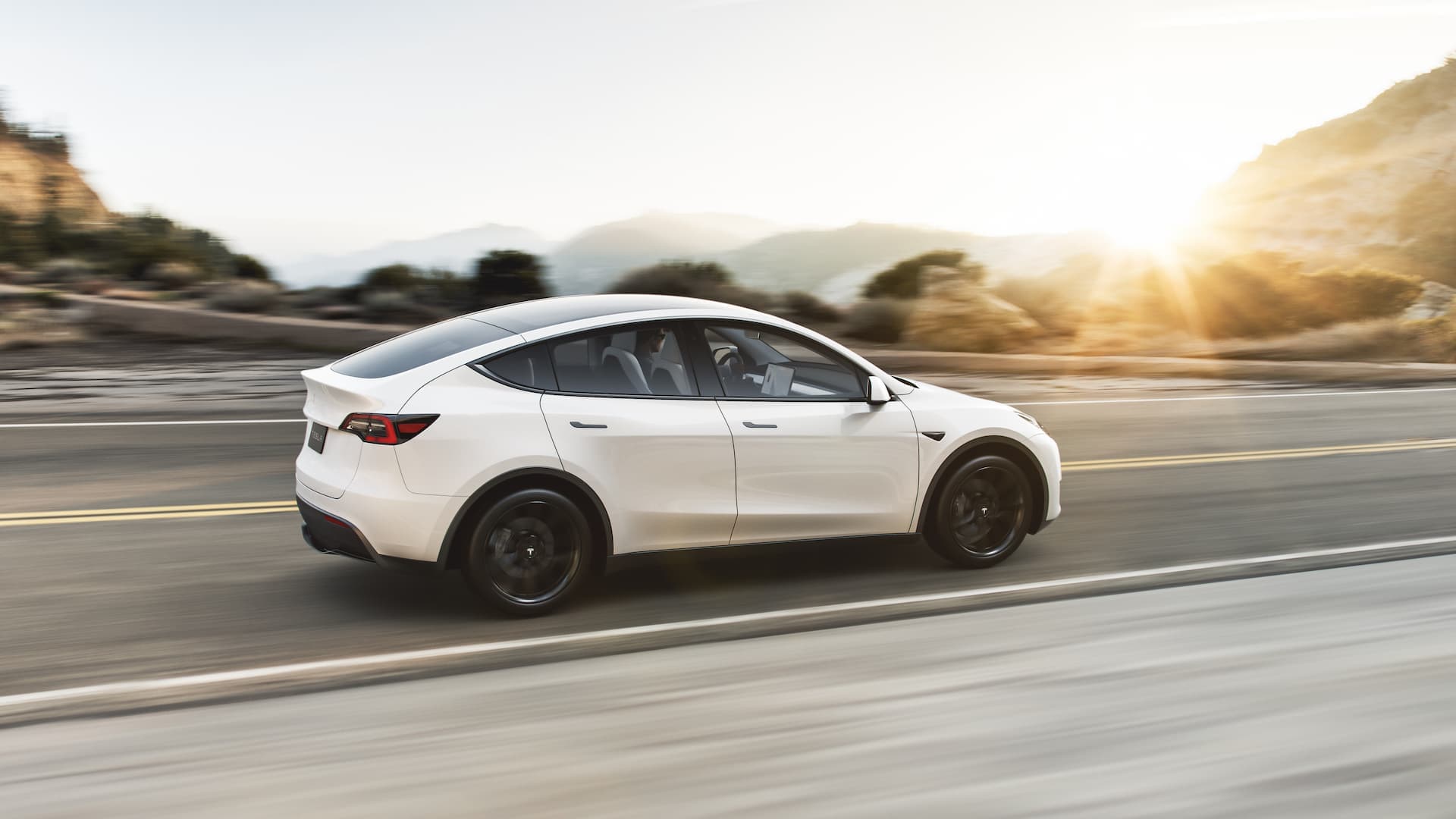 White Tesla Model Y electric SUV driving in sunset White Tesla Model Y electric SUV driving in sunset