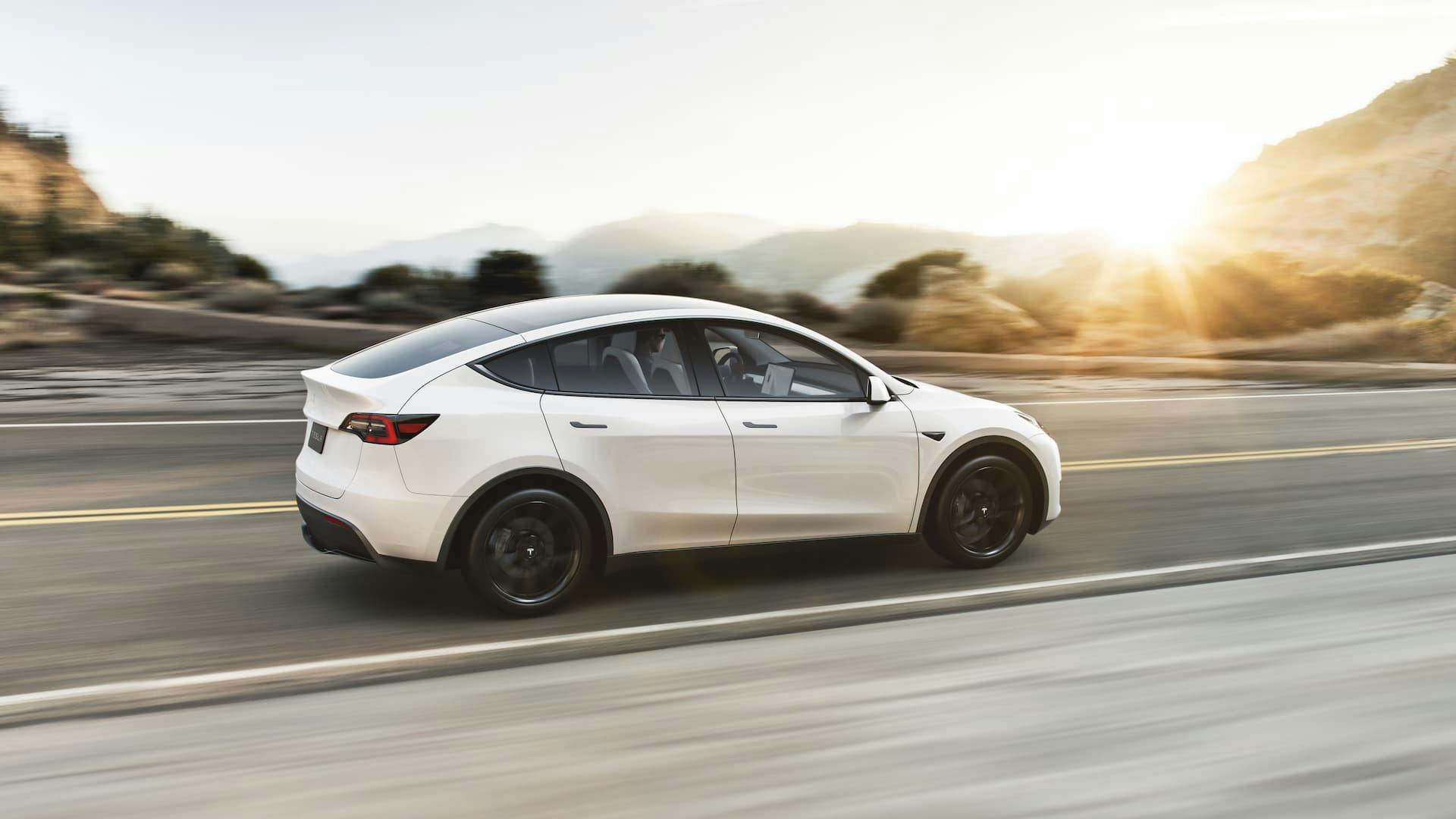 White Tesla Model Y electric SUV driving in sunset