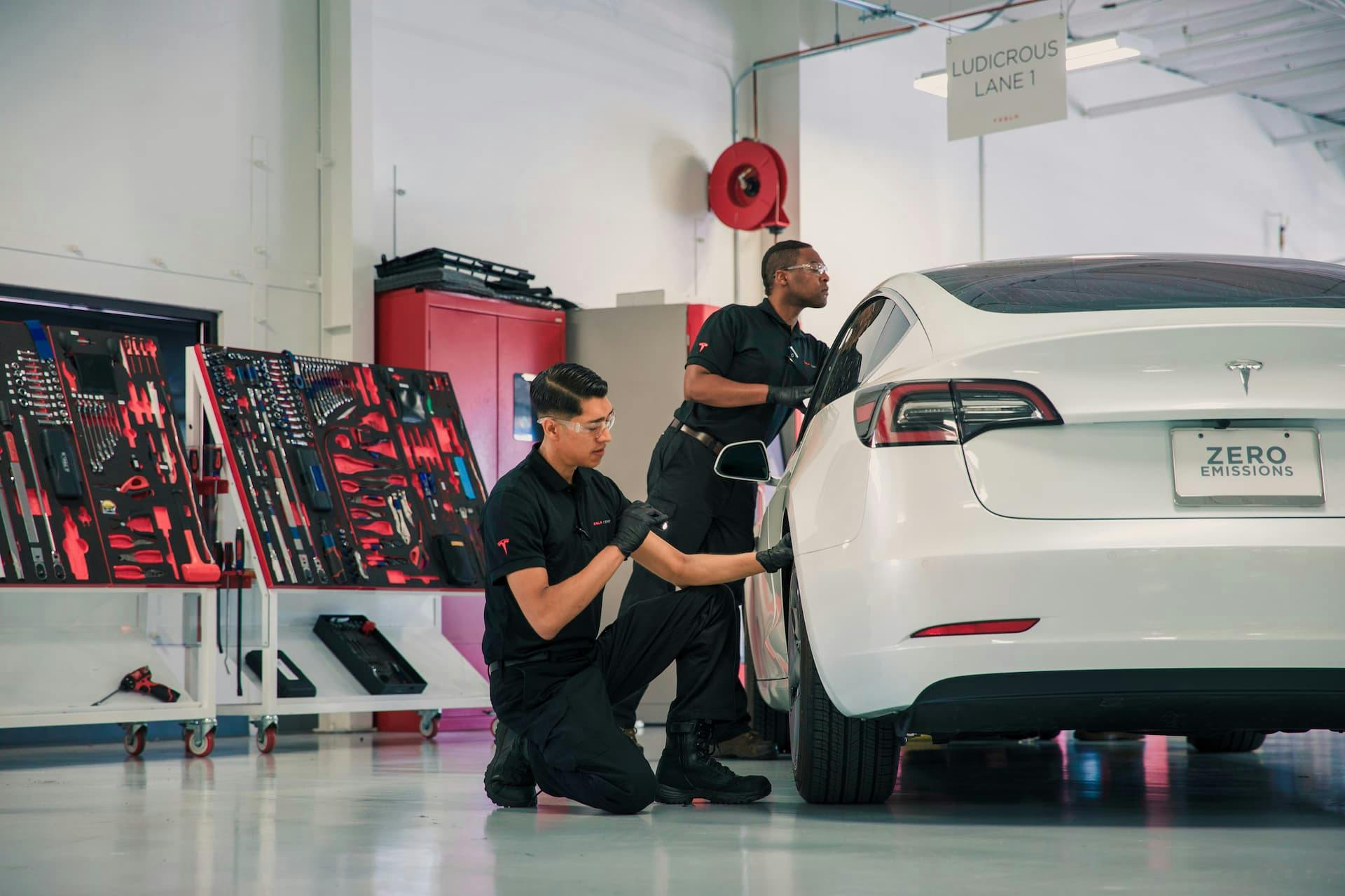 Two men inspect and service Tesla Model 3 