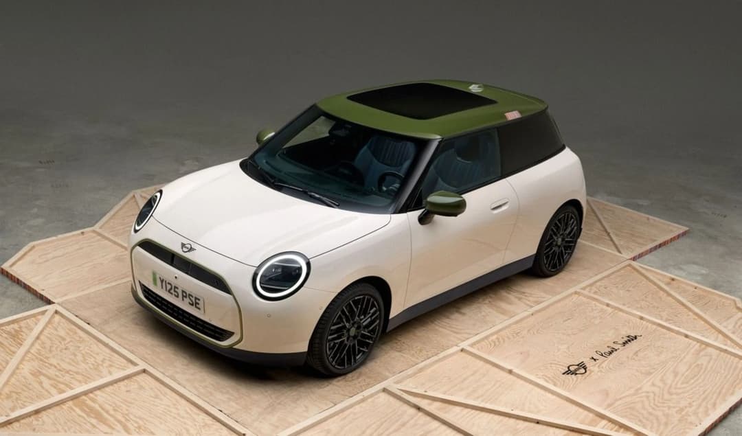 MINI Cooper SE Paul Smith Edition in white with green roof, three-quarter front view on a wooden display platform MINI Cooper SE Paul Smith Edition in white with green roof, three-quarter front view on a wooden display platform