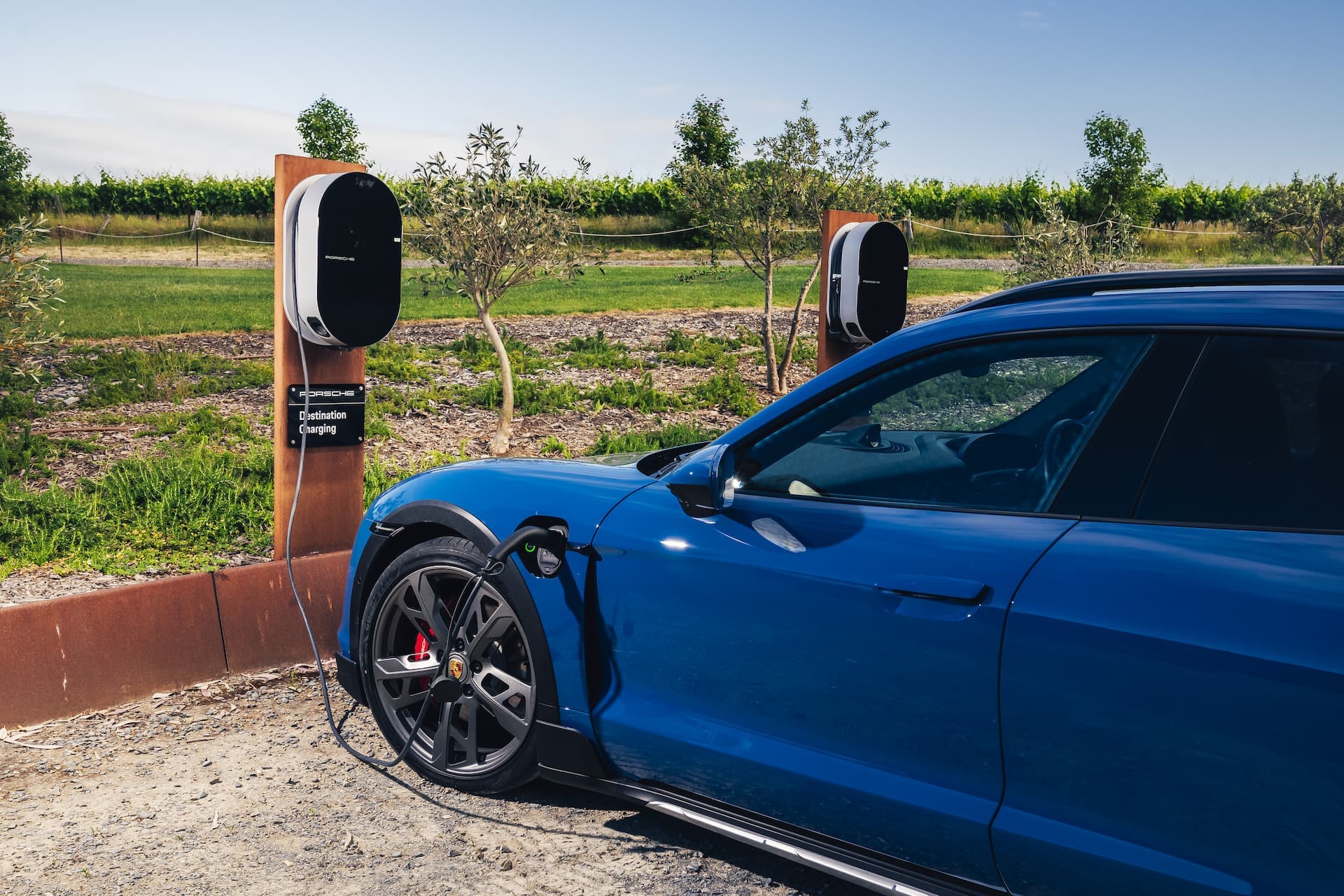 Blue Porsche Taycan Cross Turismo charging at Porsche Destination wallbox at vineyard Blue Porsche Taycan Cross Turismo charging at Porsche Destination wallbox at vineyard