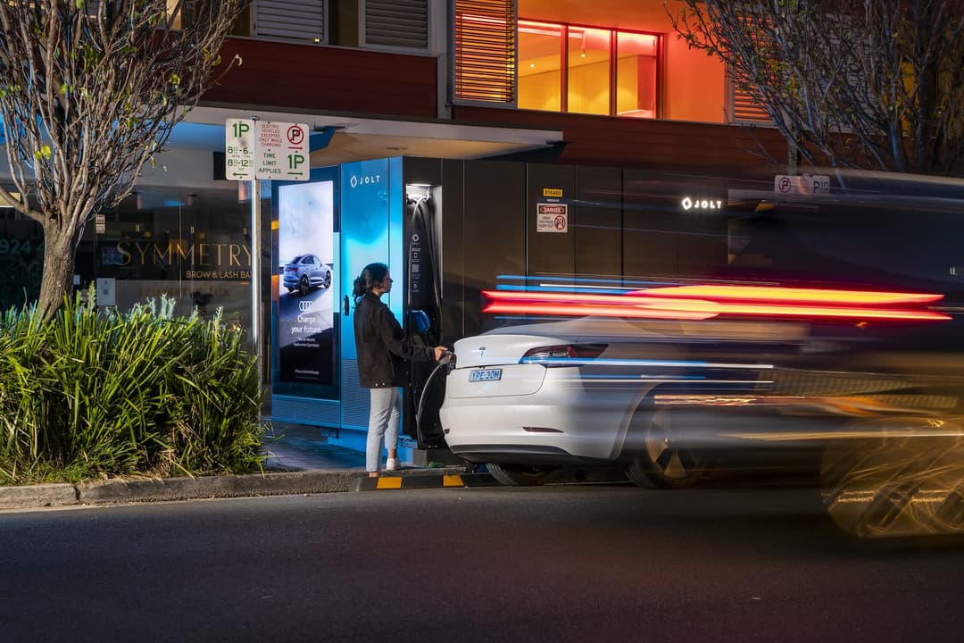 Woman plugs into Tesla Model 3 using Jolt charger at night beside street Woman plugs into Tesla Model 3 using Jolt charger at night beside street