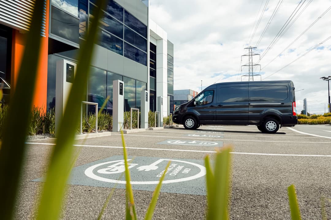 Grey Ford E-Transit at AC charging station bays in front of commercial office Grey Ford E-Transit at AC charging station bays in front of commercial office