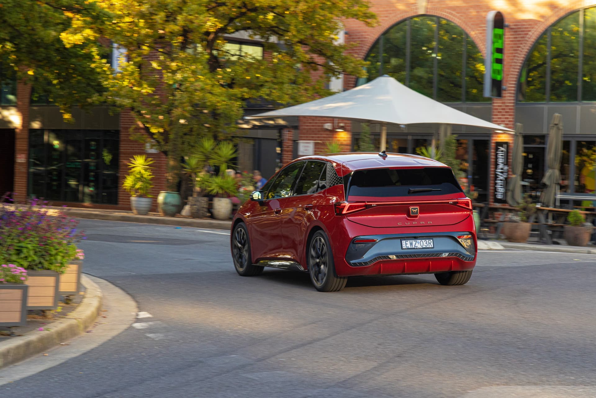 Red Cupra Born driving past cafe rear view Red Cupra Born driving past cafe rear view