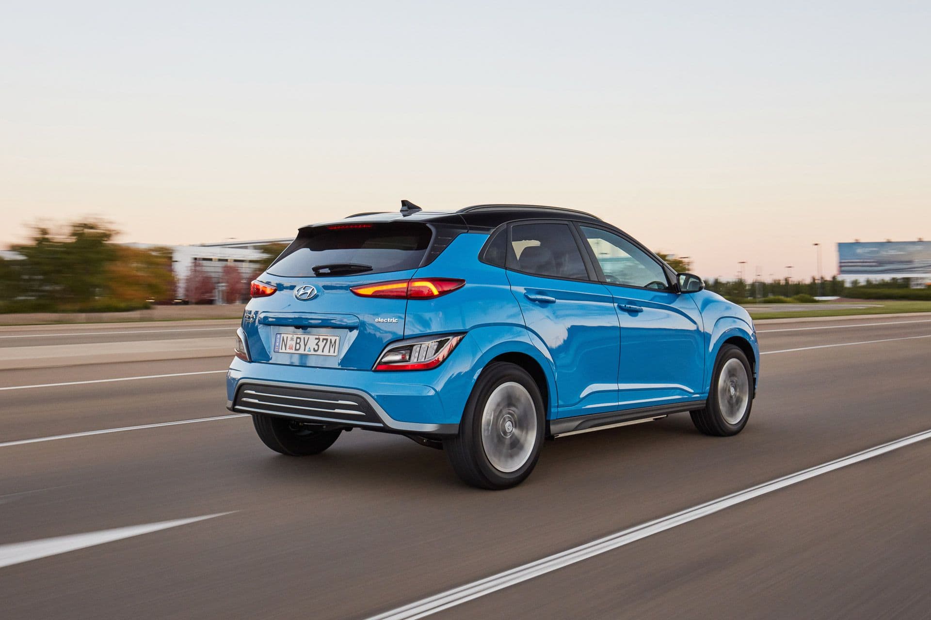 Blue Hyundai Kona Electric driving in sunset rear view Blue Hyundai Kona Electric driving in sunset rear view