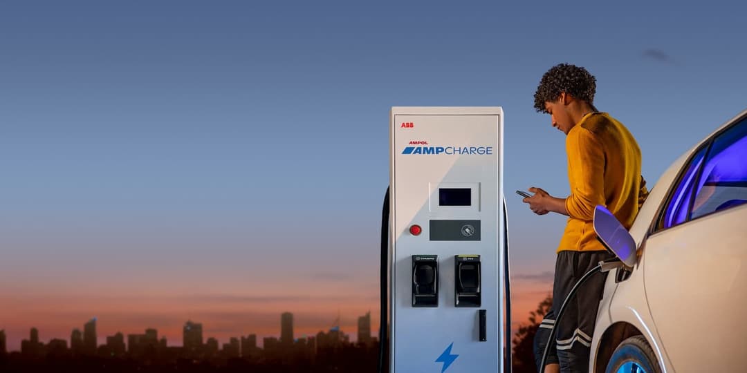Man using phone leaning on electric car in front of AmpCharge ABB charger Man using phone leaning on electric car in front of AmpCharge ABB charger