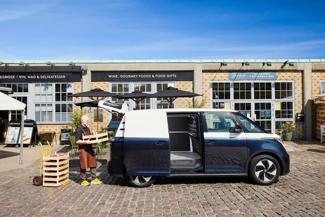 Man puts crates into Volkswagen ID.Buzz Cargo in front of gourmet shop Man puts crates into Volkswagen ID.Buzz Cargo in front of gourmet shop