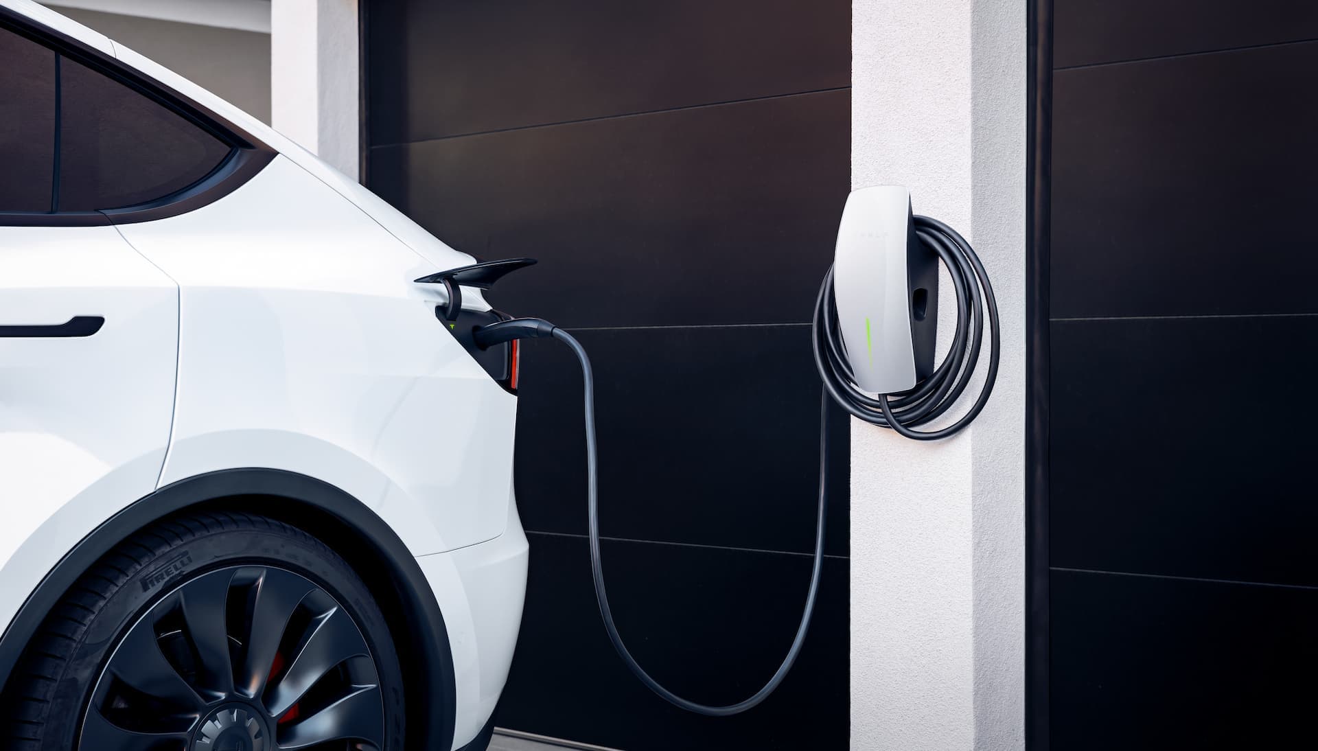 White Tesla Model Y electric SUV charging from home wallbox Tesla Wall Connector White Tesla Model Y electric SUV charging from home wallbox Tesla Wall Connector