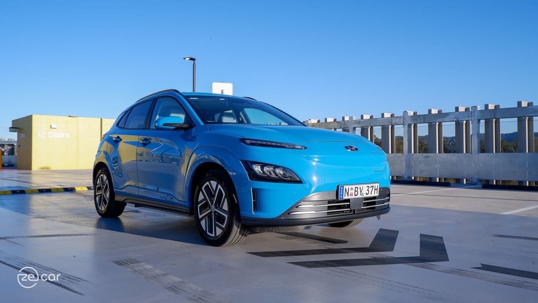 Blue Hyundai Kona Electric in front of chevron arrows in car park Blue Hyundai Kona Electric in front of chevron arrows in car park