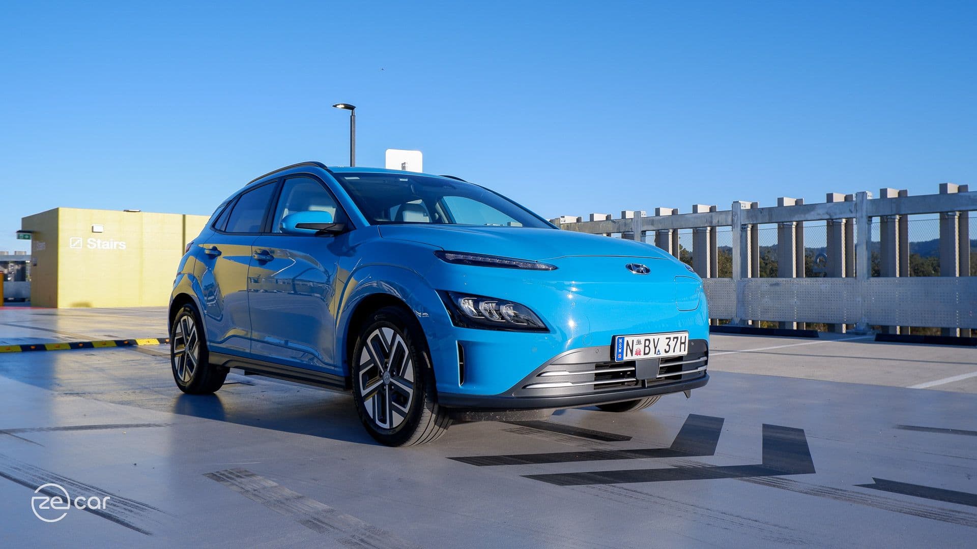 Blue Hyundai Kona Electric in front of chevron arrows in car park Blue Hyundai Kona Electric in front of chevron arrows in car park