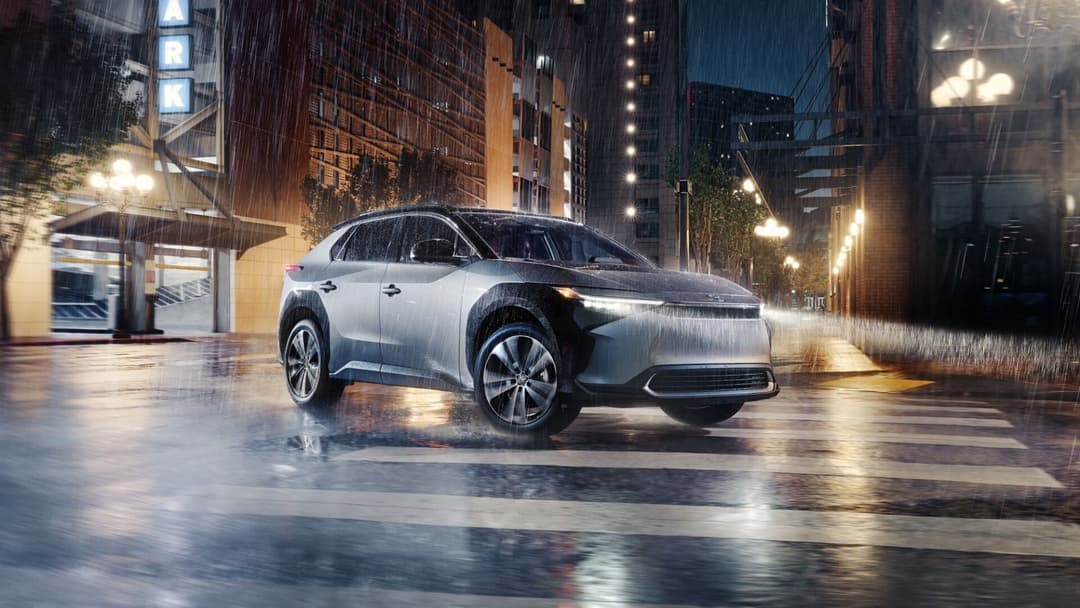 Toyota bZ4X in silver grey driving in city during rain three quarter view Toyota bZ4X in silver grey driving in city during rain three quarter view