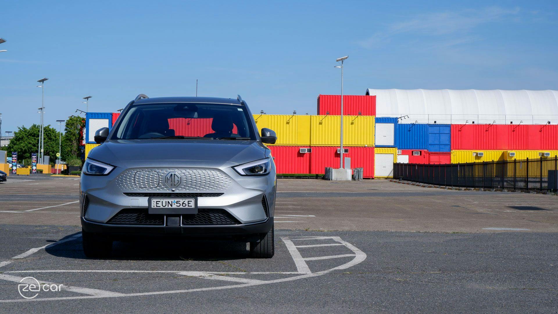 Silver MG ZS EV in front of colourful shipping containers