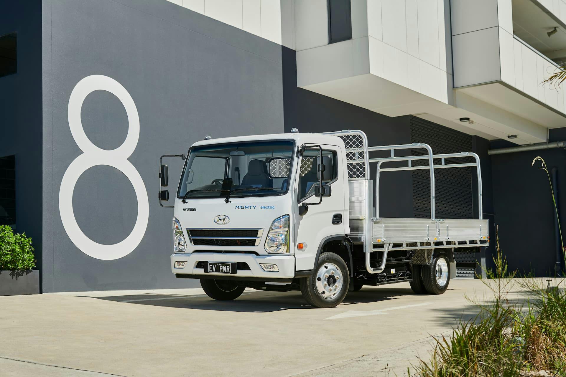 White Hyundai Mighty cab-chassis truck in front of '8' apartment symbol