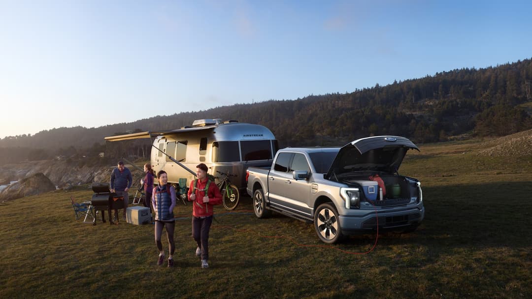 Ford F-150 Lightning ute towing caravan with open frunk and vehicle-to-load at camp site Ford F-150 Lightning ute towing caravan with open frunk and vehicle-to-load at camp site