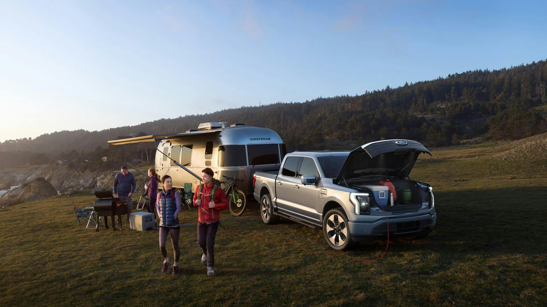 Ford F-150 Lightning ute towing caravan with open frunk and vehicle-to-load at camp site