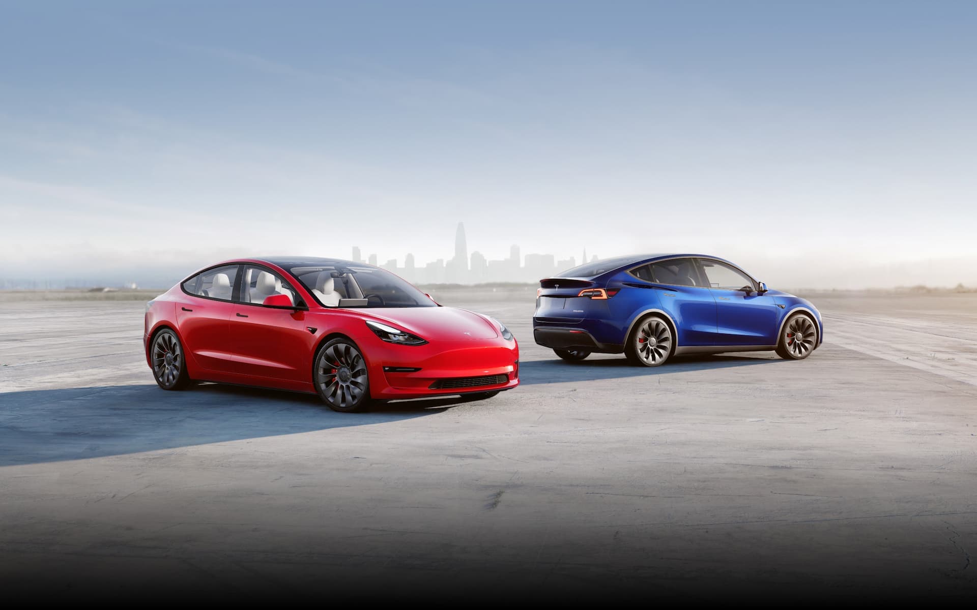 Red Tesla Model 3 and blue Tesla Model 3 in front of city Red Tesla Model 3 and blue Tesla Model 3 in front of city