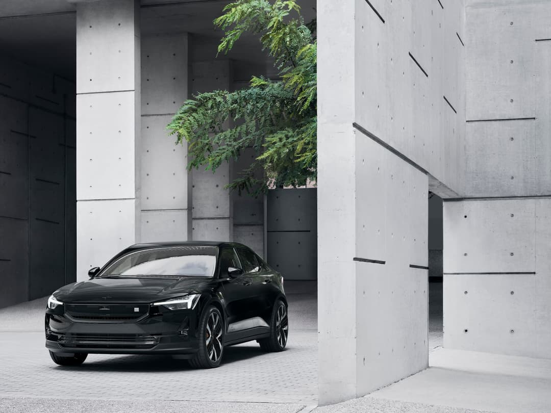 Black 2024 Polestar 2 in front of concrete and tree Black 2024 Polestar 2 in front of concrete and tree