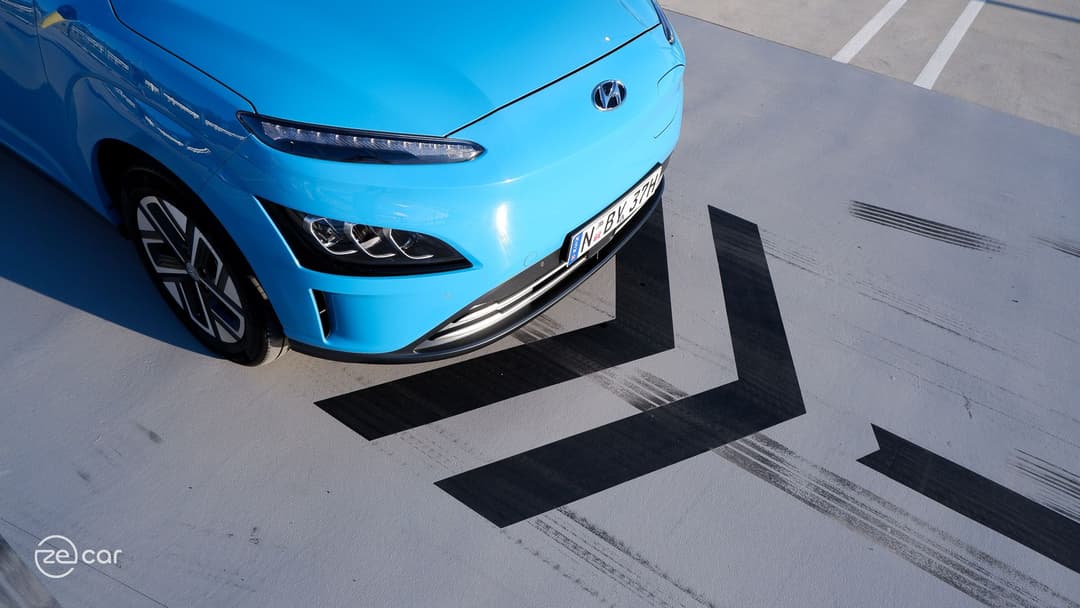 Blue Hyundai Kona Electric in front of two forward chevron arrows on the ground top view Blue Hyundai Kona Electric in front of two forward chevron arrows on the ground top view