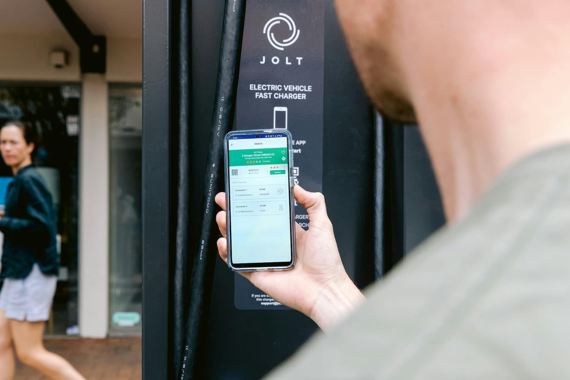 Man holding phone to use Jolt EV charging station