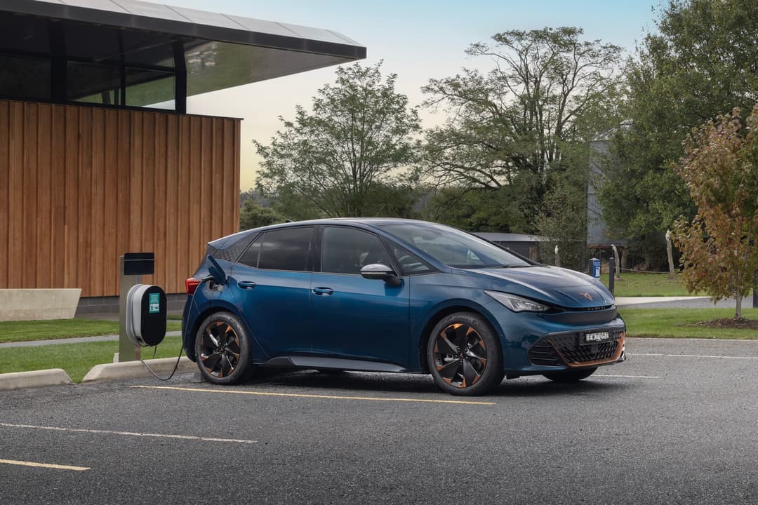 Blue Cupra Born charging from AC wall box station in front of modern building Blue Cupra Born charging from AC wall box station in front of modern building