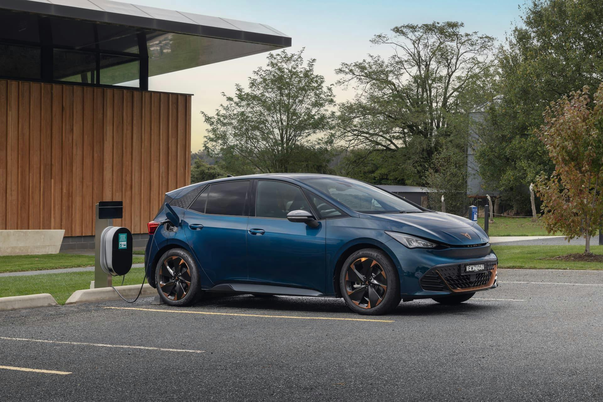 Blue Cupra Born charging from AC wall box station in front of modern building