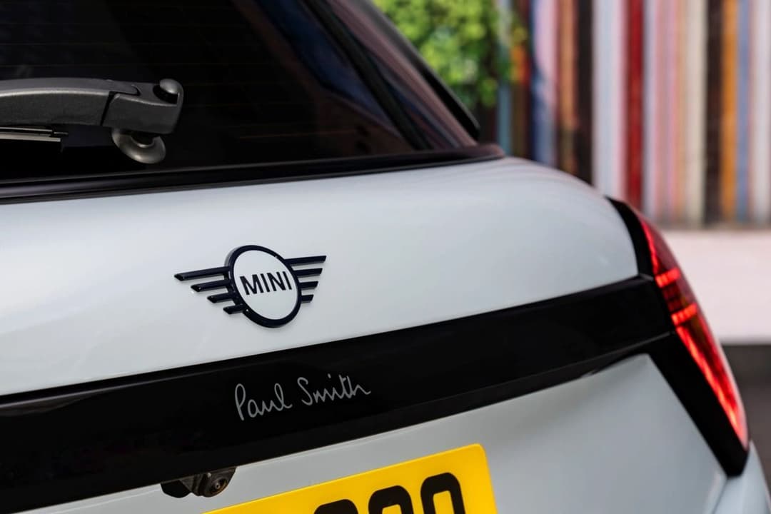 MINI Cooper SE Paul Smith Edition rear badge detail showing Paul Smith signature on black trim, outdoor urban setting MINI Cooper SE Paul Smith Edition rear badge detail showing Paul Smith signature on black trim, outdoor urban setting