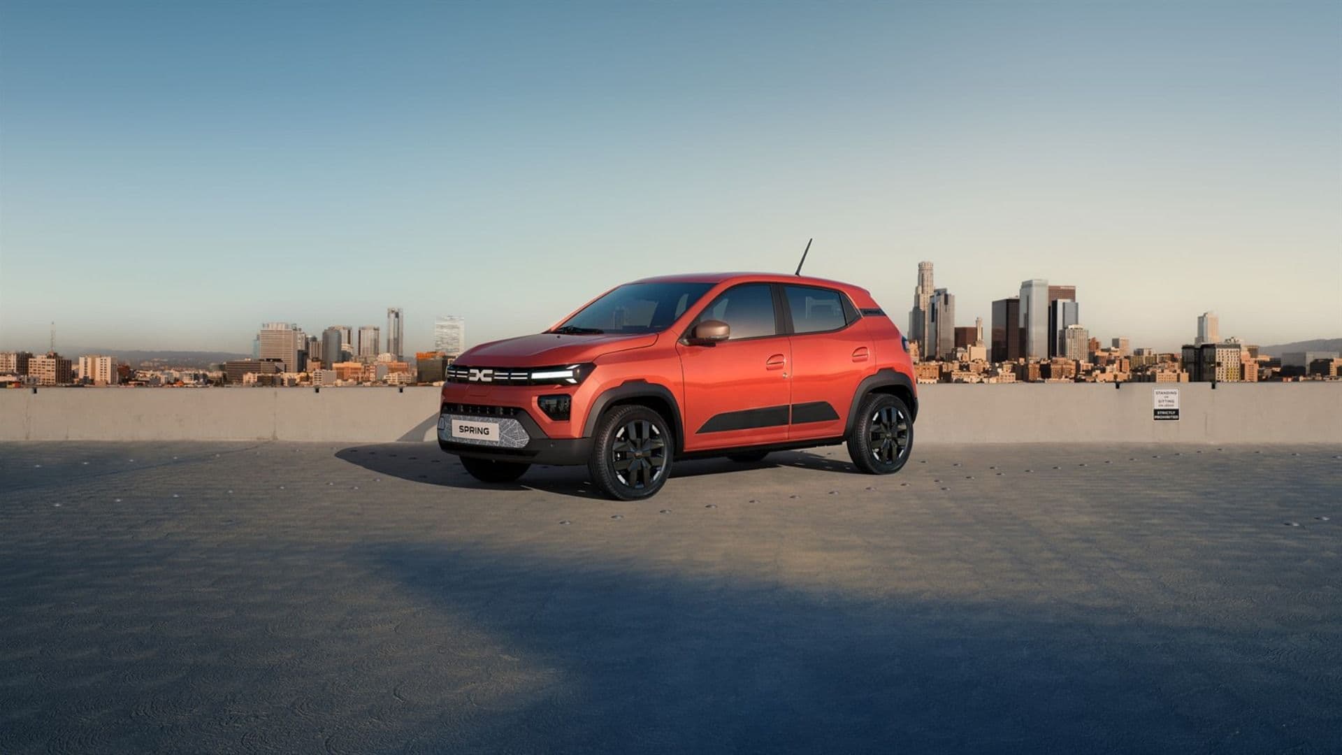 Dacia Spring three quarter view in orange parked with city skyline background Dacia Spring three quarter view in orange parked with city skyline background