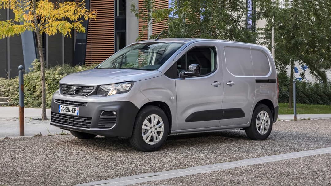 Grey Peugeot e-Partner in gravel parking lot in front of building Grey Peugeot e-Partner in gravel parking lot in front of building