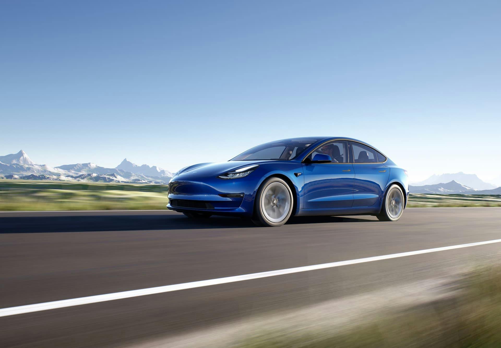 Blue Tesla Model 3 Long Range driving in front of mountains