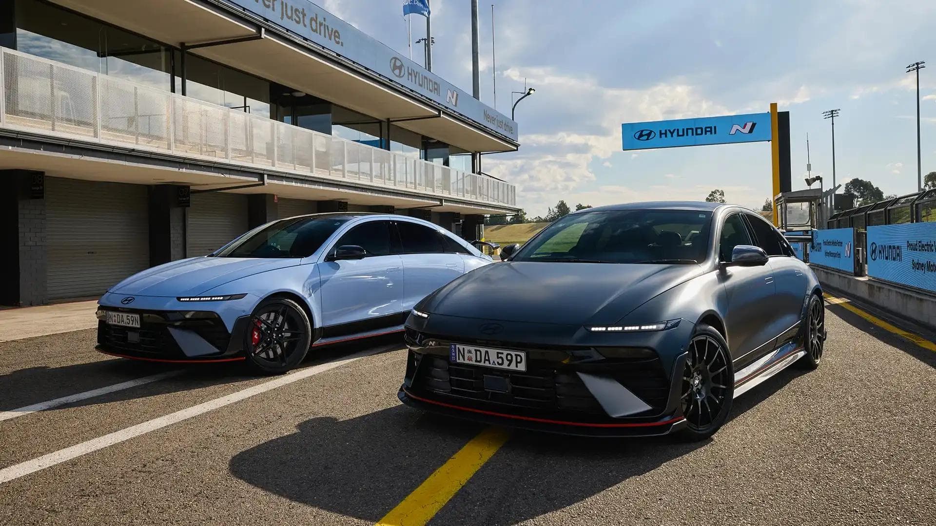 Two Hyundai N performance vehicles parked on a racetrack alongside Hyundai-branded facilities Two Hyundai N performance vehicles parked on a racetrack alongside Hyundai-branded facilities