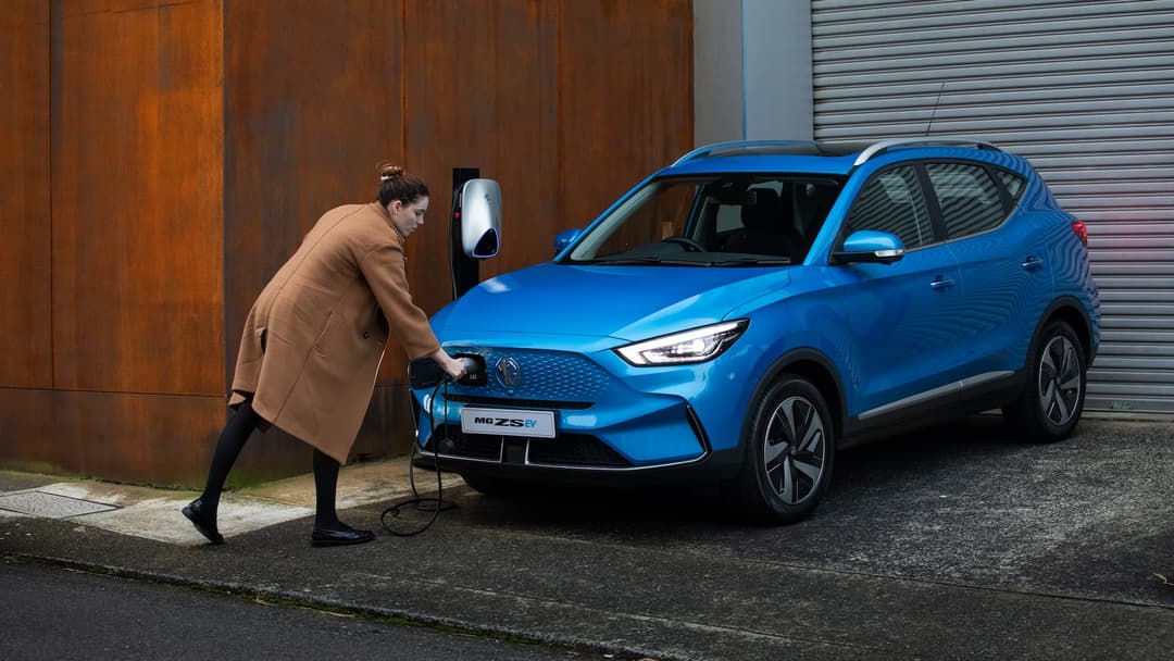 Woman plugs in charging cable into blue MG ZS EV Woman plugs in charging cable into blue MG ZS EV