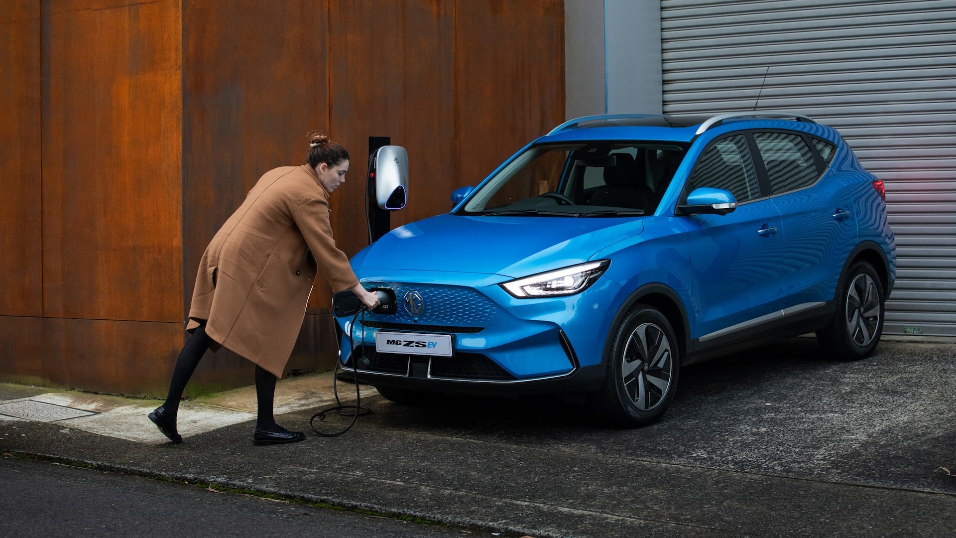 Woman plugs in charging cable into blue MG ZS EV Woman plugs in charging cable into blue MG ZS EV