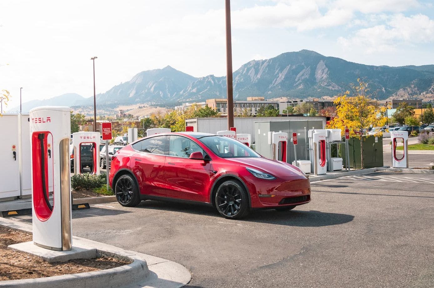 Red Tesla Model Y electric SUV charging at Supercharging station