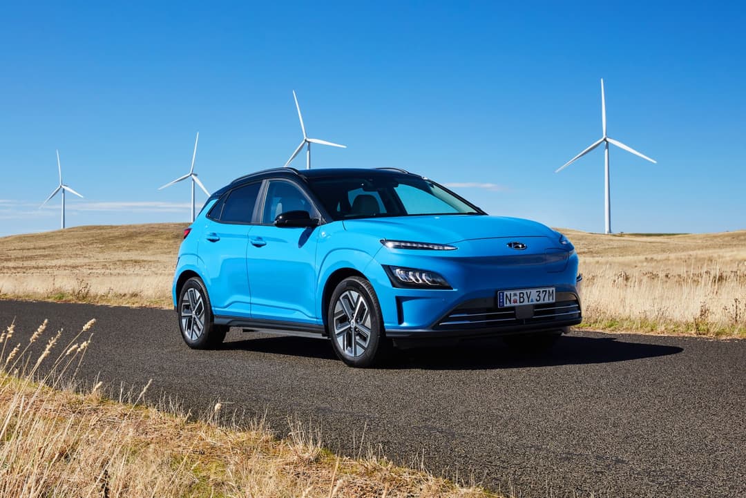 Blue Hyundai Kona Electric SUV in front of windmills Blue Hyundai Kona Electric SUV in front of windmills