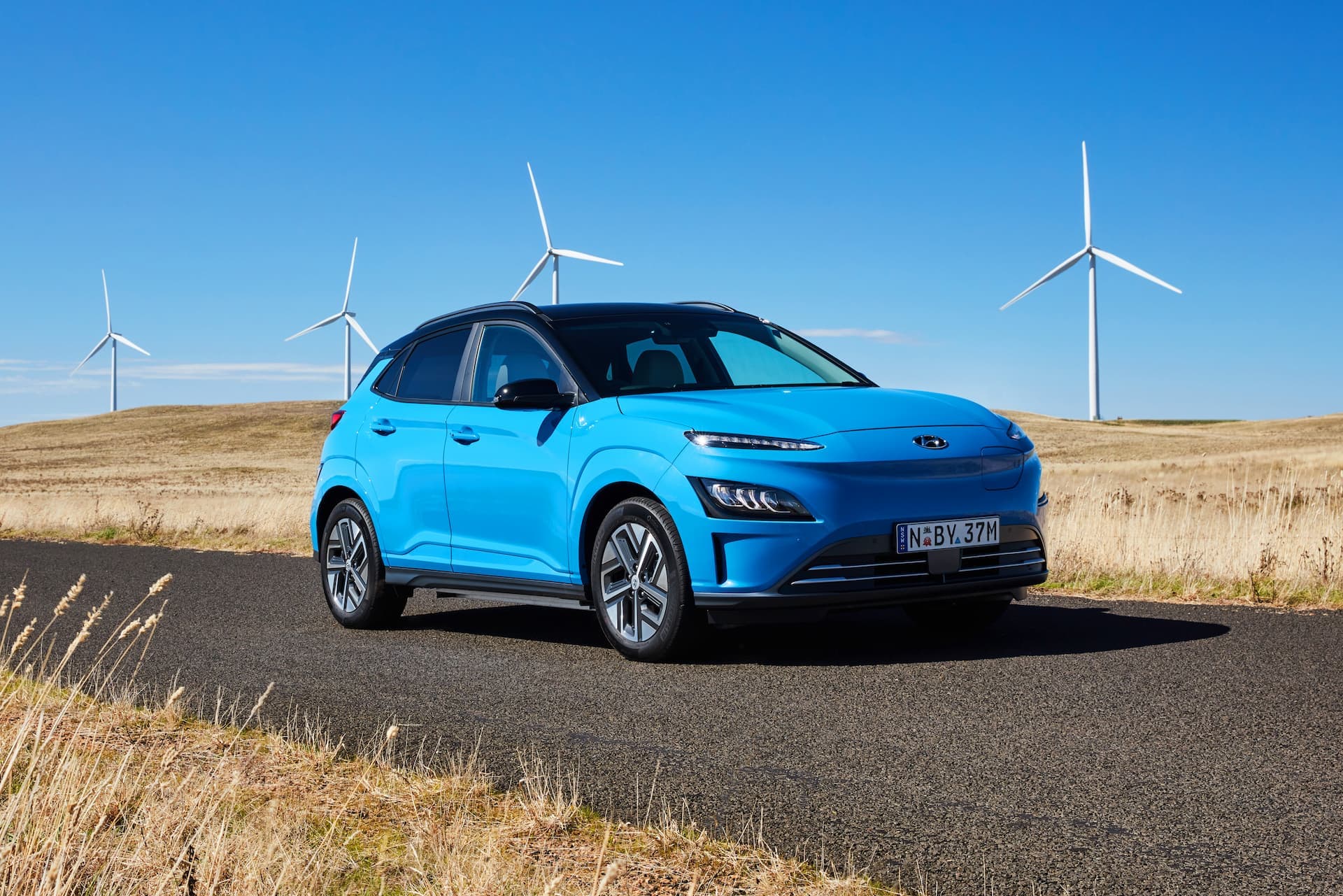 Blue Hyundai Kona Electric SUV in front of windmills Blue Hyundai Kona Electric SUV in front of windmills
