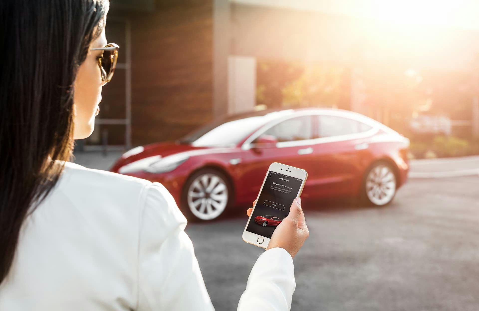 Woman uses Tesla mobile app in front of red Model 3
