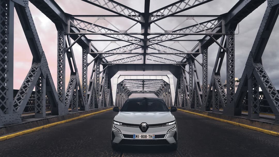 2024 Renault Megane E-Tech in grey driving on truss bridge front view 2024 Renault Megane E-Tech in grey driving on truss bridge front view