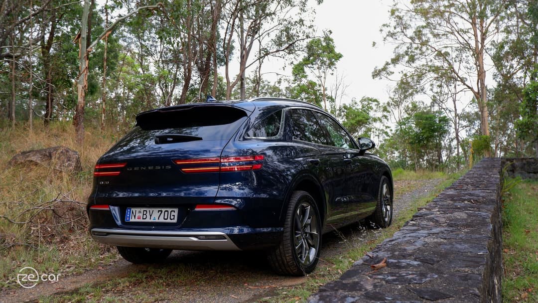 Dark blue Genesis Electrified GV70 rear three-quarter view on mountain slope Dark blue Genesis Electrified GV70 rear three-quarter view on mountain slope