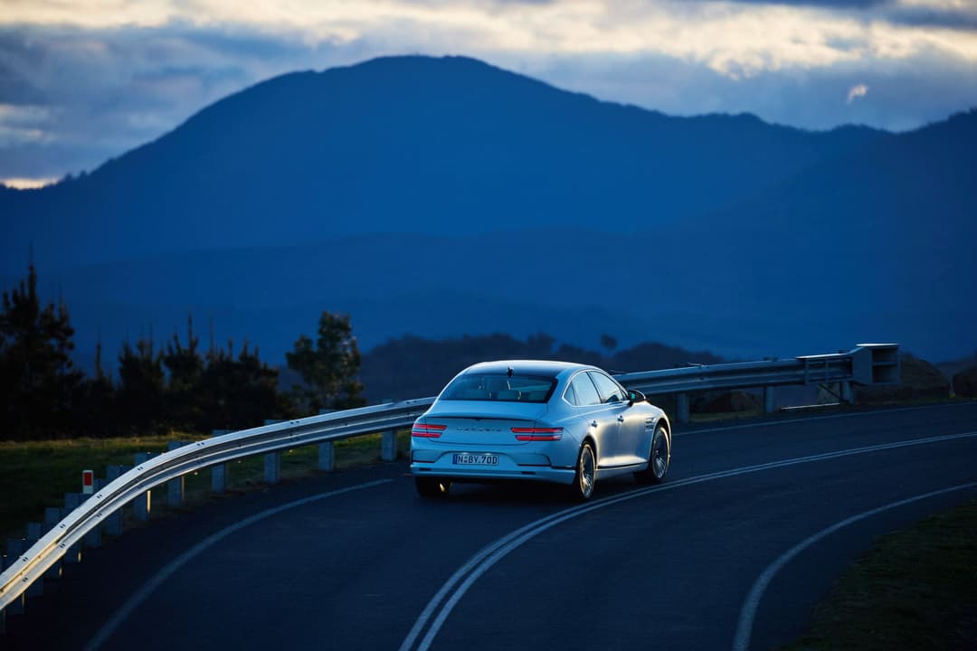 Genesis Electrified G80 driving on winding road sunset Genesis Electrified G80 driving on winding road sunset